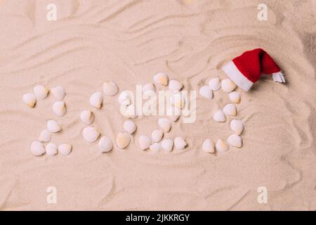 Numeri simbolici di Capodanno 2023 da conchiglie e capanno di Babbo Natale sfondo di sabbia Foto Stock