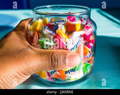 Un primo piano di una mano di un uomo che tiene un vaso di vetro pieno di caramelle colorate e dure Foto Stock