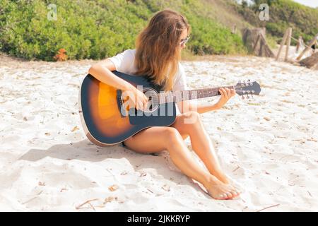 Giovane donna caucasica che suona la chitarra tra le dune della spiaggia. Foto Stock