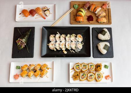 Una vista dall'alto di diversi tipi di sushi sui piatti su uno sfondo bianco Foto Stock
