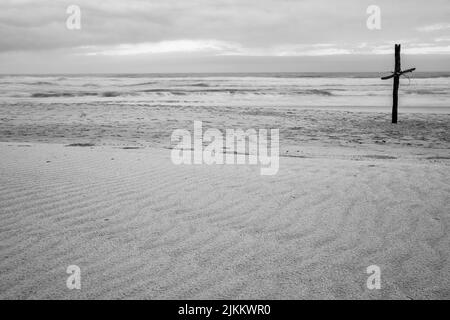 Una scala di grigi di una croce sulla spiaggia di sabbia Foto Stock