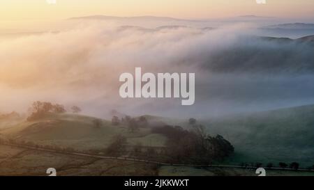 Una splendida vista panoramica della collina di Willstone coperta di nebbia pesante contro il cielo dell'alba nella mattina presto in Shropshire, Regno Unito Foto Stock