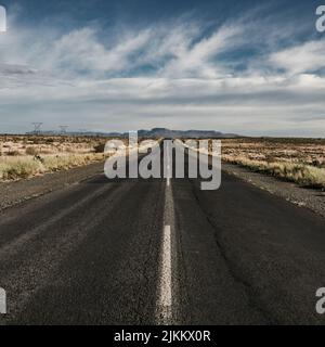 La strada asfaltata attraverso terre aride su un cielo blu nuvoloso sfondo Foto Stock