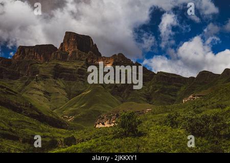 Una vista panoramica di una catena montuosa rocciosa coperta da alberi verdi e piante sotto un cielo nuvoloso blu Foto Stock