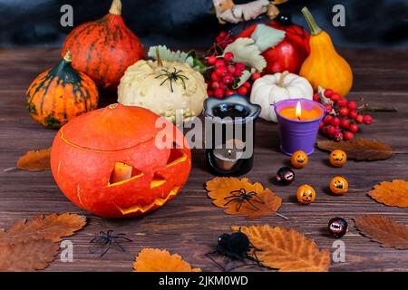 Zucche di Halloween su un tavolo di legno scuro con ragni, candele, zucche, foglie su sfondo sfocato. Messa a fuoco selettiva. Concetto di Halloween. Foto Stock