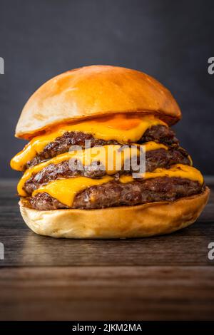 Uno shot verticale di un delizioso hamburger succoso con triplice paty su un tavolo di legno Foto Stock