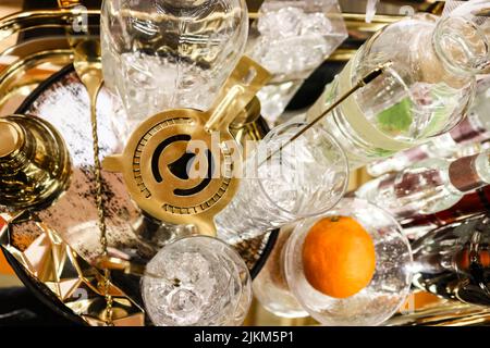 Cocktail hour - Shaker martini su vassoio con vari bicchieri e bottiglie di cristallo e una vista dall'alto arancione e fuoco selettivo Foto Stock