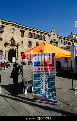 La Paz, Bolivia. 2nd agosto 2022. Una clinica medica temporanea che offre informazioni e consulenze gratuite in modo che le persone possano controllare se hanno il diabete. Il banner ha un elenco di possibili sintomi in spagnolo in modo che la gente possa decidere quanto è probabile che siano di avere il diabete. Dietro fa parte della chiesa e del convento di San Francisco, la chiesa coloniale più importante e suggestiva della città. Foto Stock