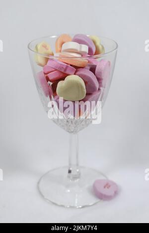 Vetro di cristallo del vino che mantiene i cuori di caramelle color pastello su uno sfondo chiaro - fuoco selettivo Foto Stock