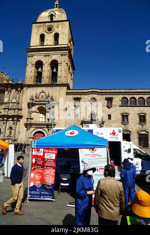 Plaza San Francisco, la Paz, Bolivia. 2nd agosto 2022. Un medico parla con un membro del pubblico vicino al centro di raccolta mobile dove le persone possono dare il sangue, un servizio organizzato dalle autorità sanitarie della città di la Paz. Le banche del sangue della Bolivia si affidano molto alle donazioni di volontari e centri di raccolta come questo sono comuni nella città, soprattutto durante i periodi di vacanza o quando ci sono carenze. Dietro si trova la chiesa di San Francisco, la più importante e suggestiva chiesa coloniale della città. Foto Stock