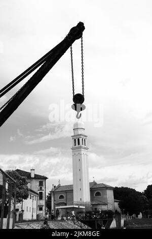 Un colpo in scala di grigi di un gancio per gru industriale con lo sfondo di un campanile Foto Stock