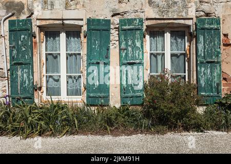 Le finestre di una vecchia casa distrutta con persiane verdi Foto Stock