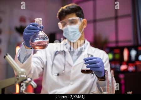 Esperto scienziato arabo maschile in industria sanitaria che fa l'analisi di sostanza utilizzando il microscopio. Ricercatore chimico in laboratorio sterile facendo esperimenti per l'industria medica utilizzando la tecnologia moderna. Foto Stock