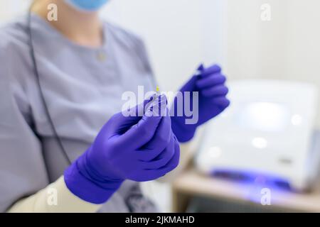 primo piano delle mani del maestro dell'elettrolisi in cui tiene un ago per rimuovere i capelli indesiderati Foto Stock