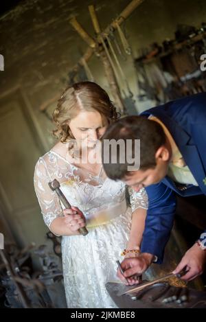 Una sposa e uno sposo caucasici in un fabbro che colpisce il metallo e incisa una data importante Foto Stock