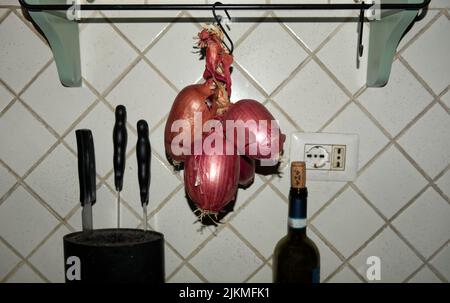 Cucina italiana: Una treccia di cipolline rosse dolci tropea appese in cucina Foto Stock