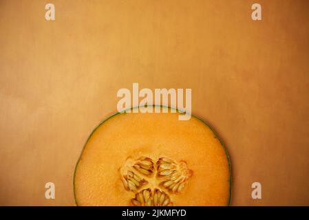 Singola fetta di cantalupo su fondo di terracotta arancione vista dall'alto metà di melone Foto Stock