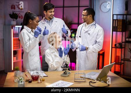 Scienziati medici internazionali professionisti che si aggrappano le mani dopo la fine dell'esperimento nel laboratorio di biologia moderna. Foto Stock