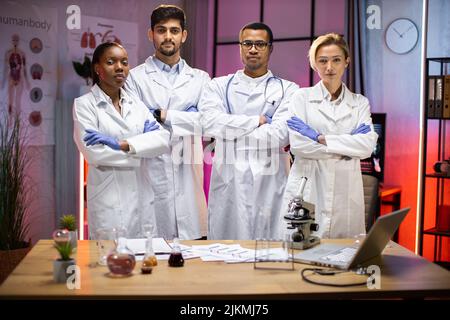 Gruppo sorridente di scienziati in laboratorio moderno con leader maschile afroamericano, mix team di ricercatori scientifici in laboratorio indossando camici bianchi e stetoscopi Foto Stock