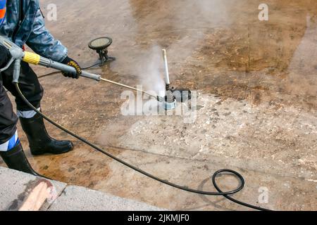 Un uomo utilizza una idropulitrice elettrica per una idropulitrice. Pulizia delle fontane della città in autunno. I lavoratori rimuovono lo sporco che si è depositato durante la s. Foto Stock