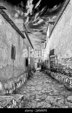 Una scala di grigi verticale di un vicolo stretto e vuoto in una piccola città del Marocco Foto Stock