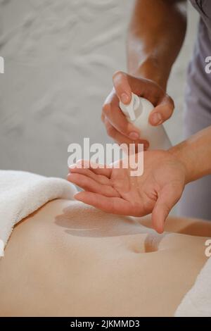 le mani del massaggiatore versano l'olio aromatico sulla schiena della donna. Massaggiatrice preparatevi a fare la procedura termale orientale per un trattamento rilassante. Terapista che fa olio di aromaterapia Foto Stock