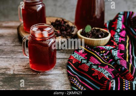 Agua de Jamaica o roselle mocktail drink, bevanda estiva in messico con ghiaccio e petali di ibisco secco sullo sfondo del tavolo Foto Stock