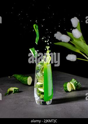 Un vivace shot estetico di un bicchiere diviso in un succo fresco e pezzi di cetriolo Foto Stock