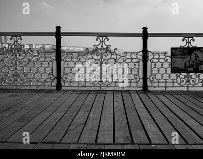 Un'immagine simmetrica in scala di grigi di un pavimento in legno e recinzione metallica sul Brighton Pier nel Regno Unito Foto Stock