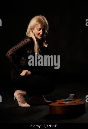 donna bionda con chitarra in studio su sfondo nero Foto Stock