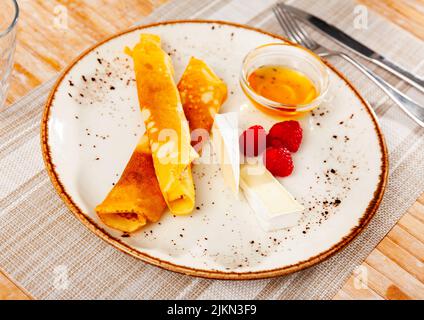 Pancake sottili con fette di brie, lamponi e miele Foto Stock