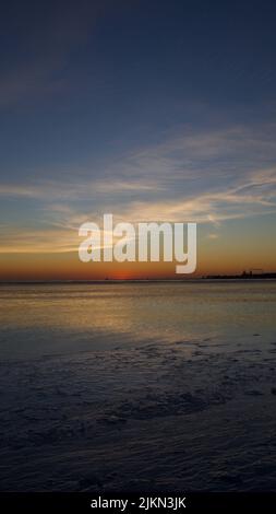 Uno scatto verticale di un tramonto ipnotico sull'orizzonte e sulle onde del mare Foto Stock