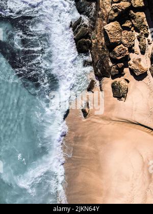 Una foto aerea di una spiaggia rocciosa con belle onde blu e sabbia fine Foto Stock