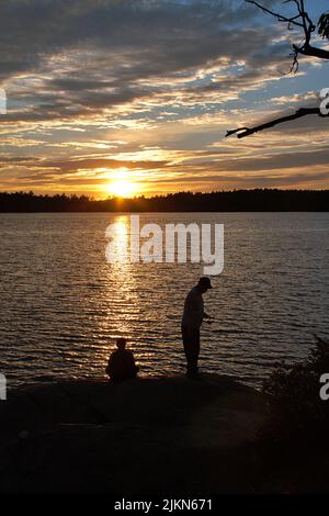 Uno scatto verticale di un pescatore di sagome sulla riva di un lago al tramonto Foto Stock