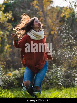 Donna in maglione rosso ballando felicemente su un prato in una foresta in autunno. Foto Stock