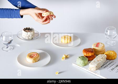 Una persona seduta ad un tavolo da caffè con vari tipi di dessert su uno sfondo bianco Foto Stock