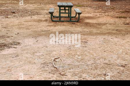 Una panca di legno vuota con tavolo in campo arido di un parco Foto Stock