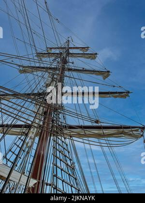 L'alto albero di una vecchia nave a vela con una scala a fune sullo sfondo blu del cielo Foto Stock