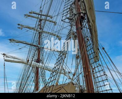 L'alto albero di una vecchia nave a vela con una scala a fune sullo sfondo blu del cielo Foto Stock