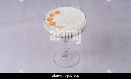 Un primo piano di un cocktail Pisco acido in una classe su una superficie bianca. Foto Stock