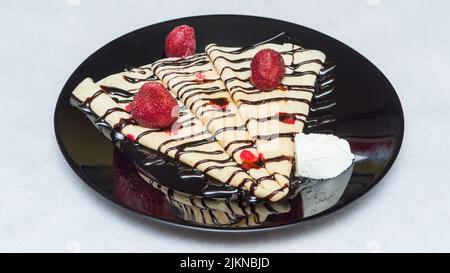 Un primo colpo di crepes con sciroppo al cioccolato e fragole su un piatto nero Foto Stock