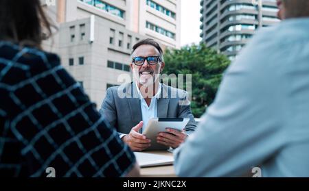 Ha sicuramente grandi idee da condividere. Un uomo d'affari maturo che usa un tablet digitale durante una riunione con i suoi colleghi sul balcone di un ufficio. Foto Stock