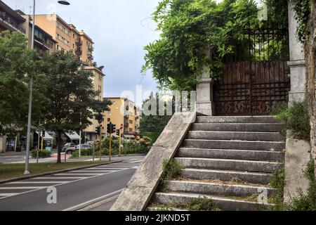 Scala in pietra usurata che conduce ad un cancello arrugginito vicino ad un muro di pietra in una giornata nuvolosa Foto Stock