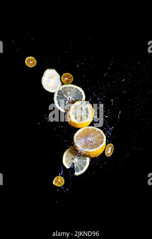 Molte fette di limone e lime spruzzano e galleggiano su uno sfondo nero Foto Stock