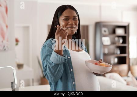 La mamma e il bambino hanno bisogno di mangiare sano troppo. Ritratto di una donna incinta che mangia una ciotola di frutta a casa. Foto Stock