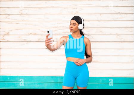 Una donna afro-americana che indossa abbigliamento sportivo e cuffie per scattare una foto con la fotocamera del telefono Foto Stock