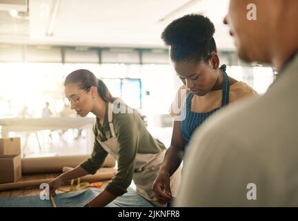 Gruppo di design, stile e moda impegnato a lavorare con tessuti di design all'interno di una struttura di officina. Lavoratori di fabbrica diversi, donne di produzione e. Foto Stock