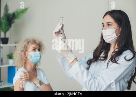 Medico che tiene una siringa con vaccini liquidi contro il virus covid-19 per gli adulti. Vaccinazione contro il coronavirus. Prevenzione delle pandemie. Foto Stock