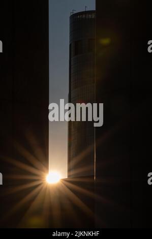 Uno scatto verticale del sole che splende attraverso gli edifici al tramonto Foto Stock