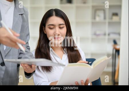 Attraente giovane dipendente asiatico di lavoro e di revisione di alcune informazioni sul rapporto con il suo team. Foto Stock